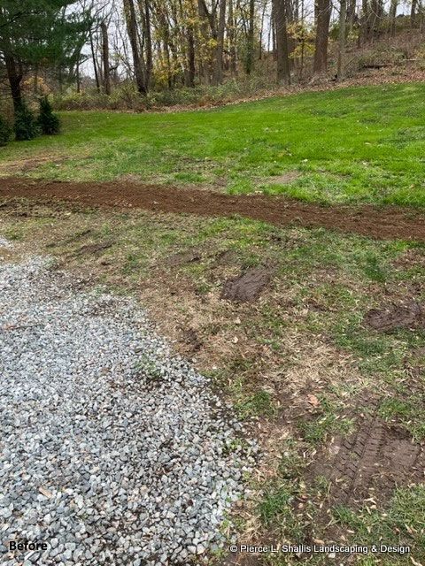 Gravel drive beside a grassy yard and dirt path, with trees in the background.