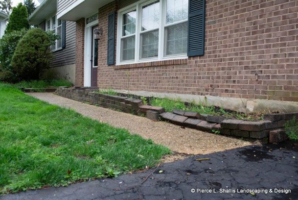 Brick house with a sloped gravel walkway and a cracked, sunken concrete edge along the foundation