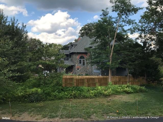 Stone house behind wooden fence amid green trees under a cloudy blue sky