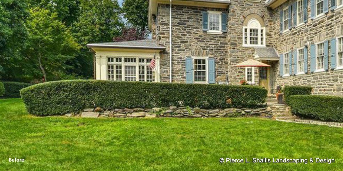 Stone house with blue shutters, trimmed hedges, and a green lawn in front.