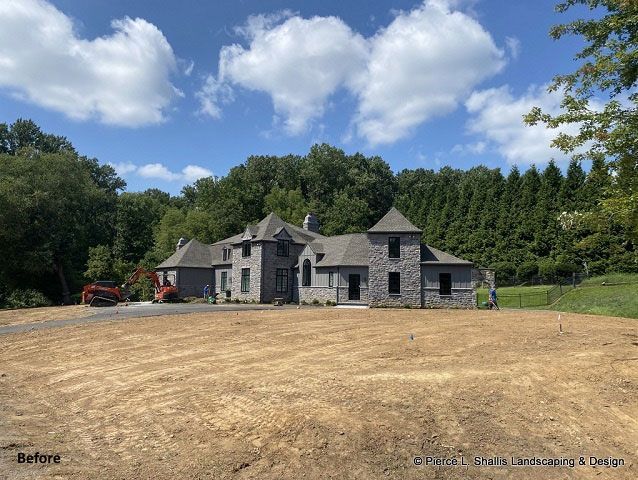 Stone house under construction on a cleared lot with trees and blue sky