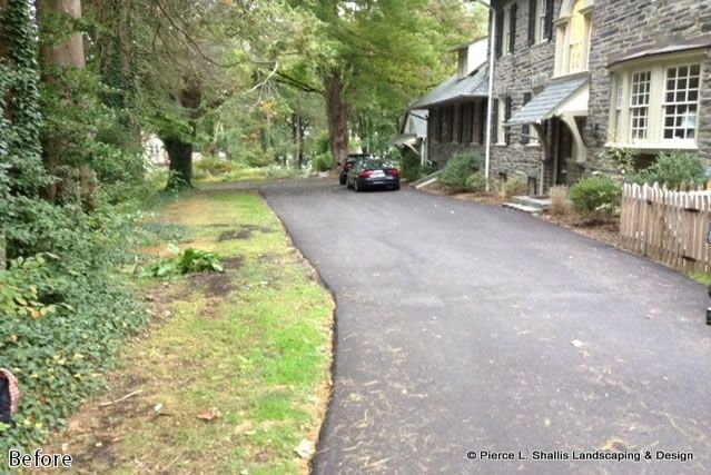 Driveway beside a stone house and wooded garden, with a parked car in the distance.