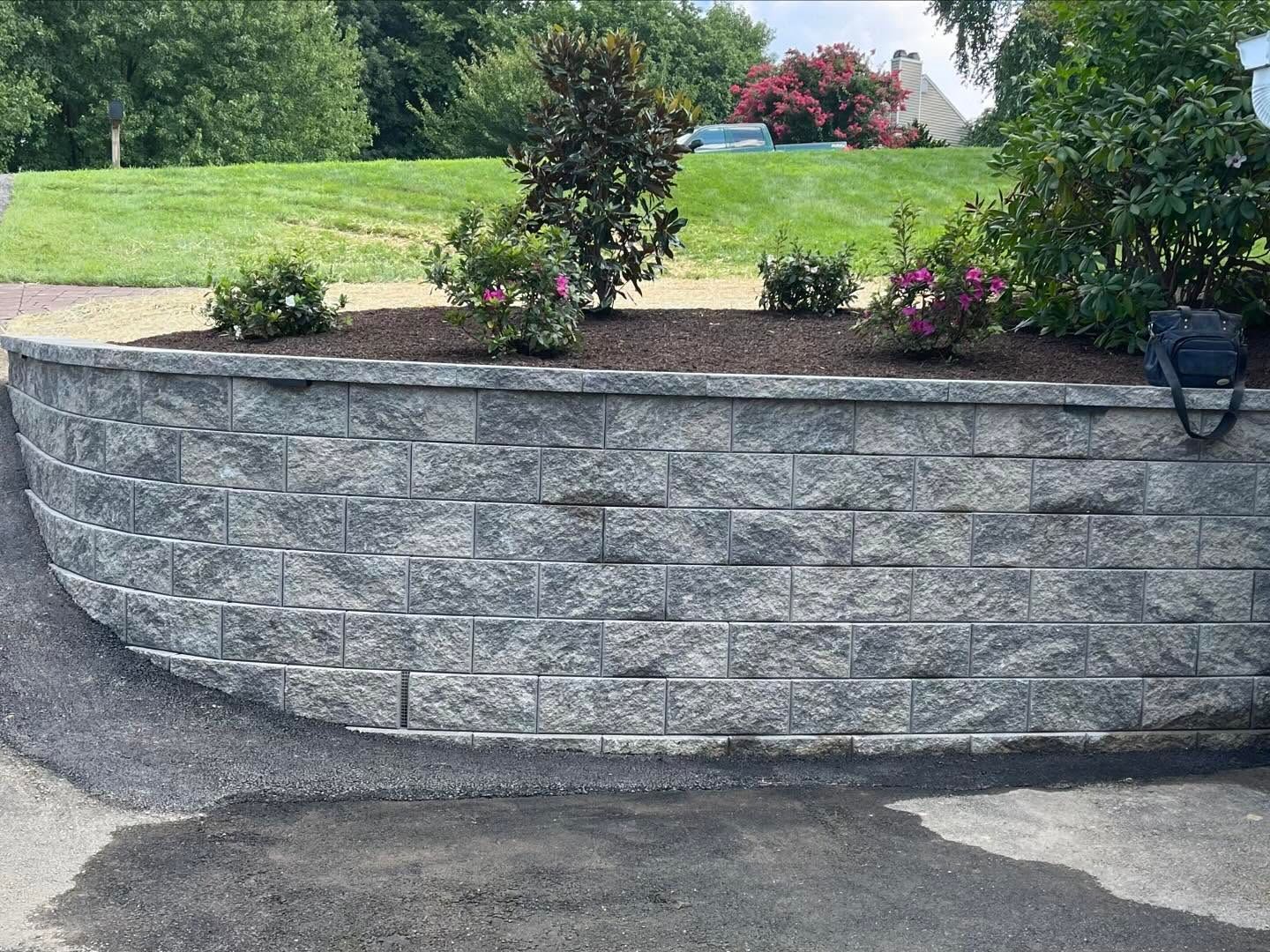 Curved stone retaining wall with small flowering shrubs in a landscaped garden by a paved drive