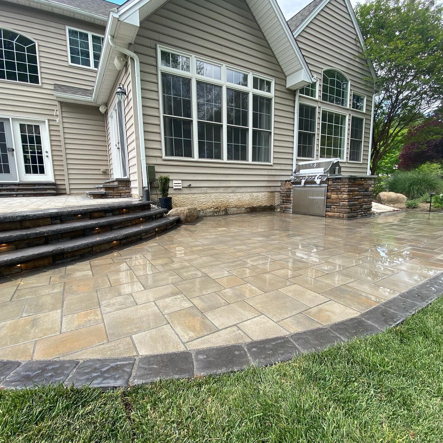 Stone patio and steps beside a beige house after rain, with water pooling on the patio.