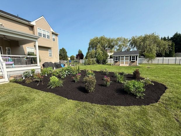 Front yard landscaping with a newly planted flower bed, green lawn, and a house with a porch.
