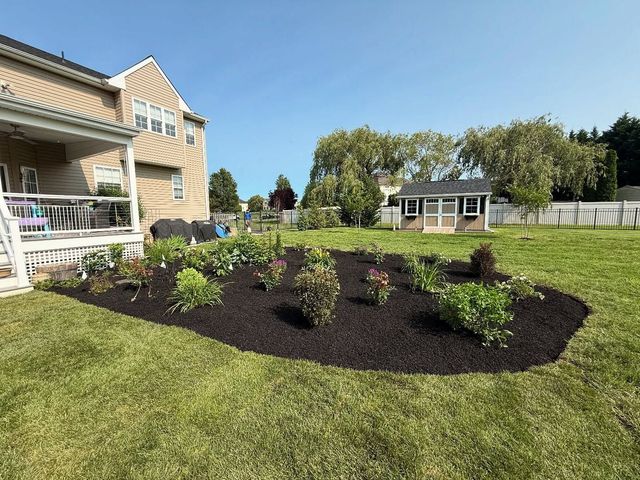Front yard landscaping with a newly planted flower bed, green lawn, and a house with a porch.
