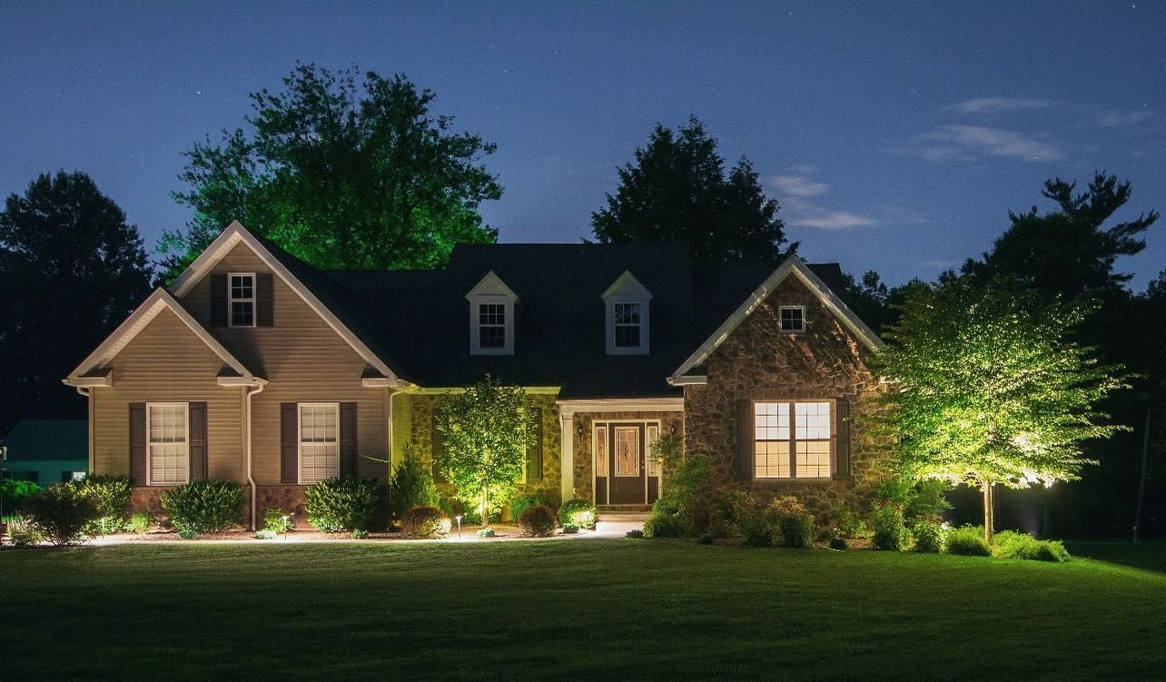 Well-lit suburban house at night with glowing windows and trees in the front yard