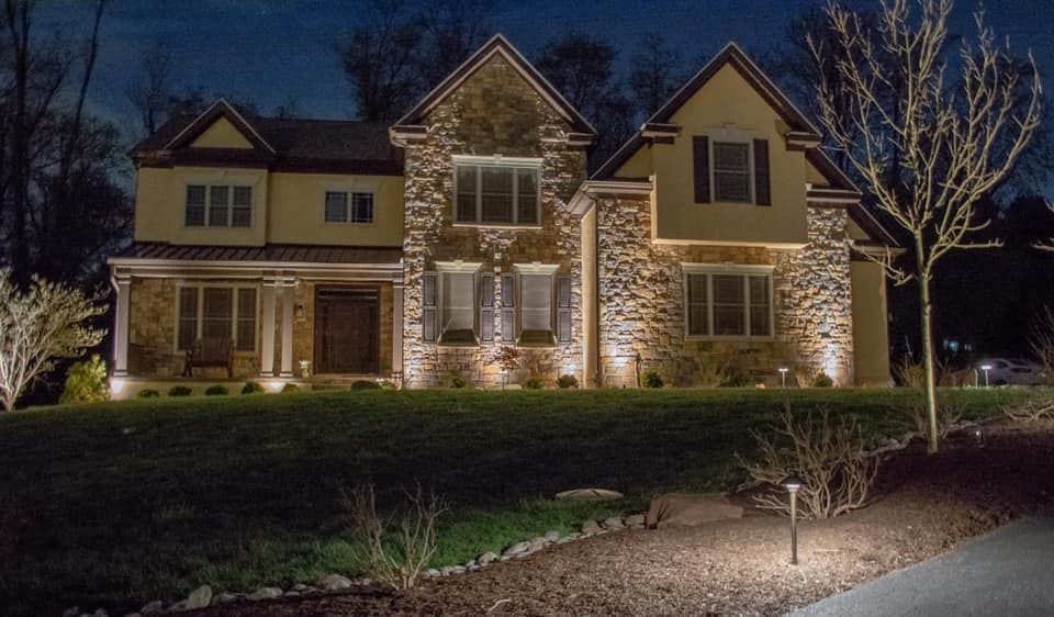 Large stone house at night with warm exterior lights and a lit front yard path.
