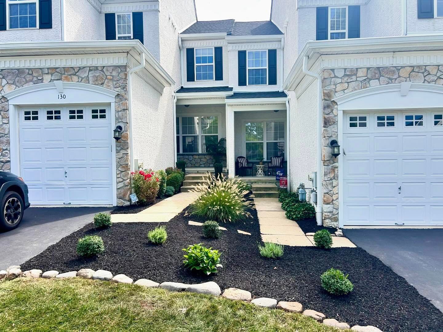 Two-story townhouses with white garage doors and a landscaped front walkway of black mulch and shrubs