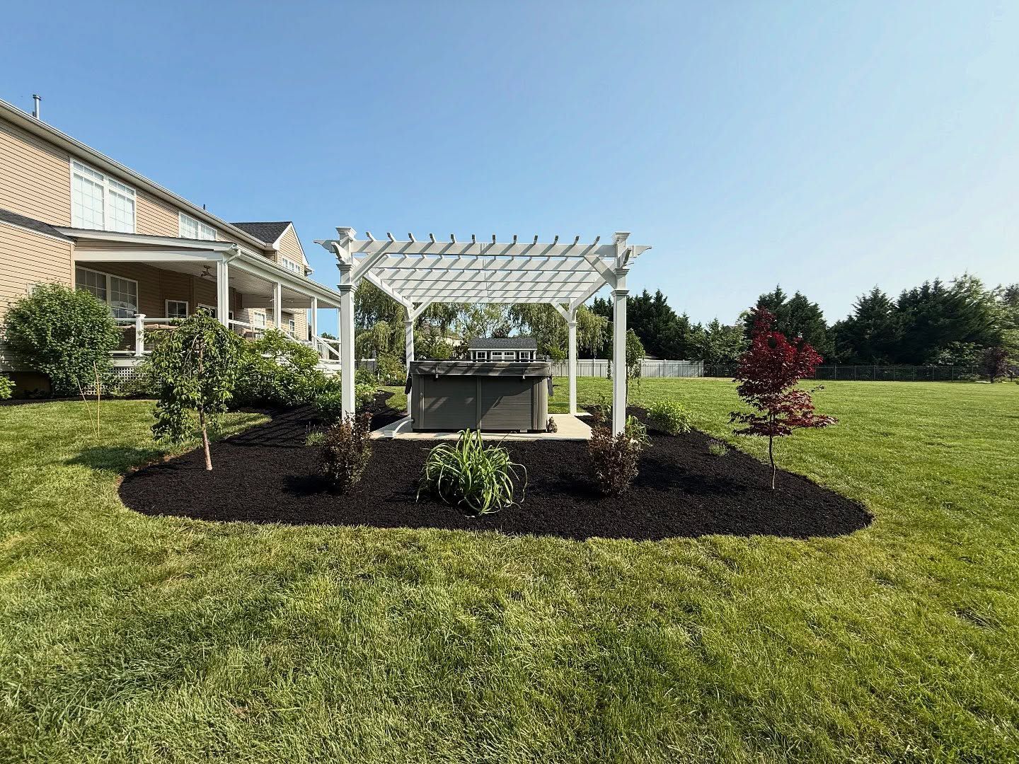 Backyard pergola garden with fresh mulch, lawn, and a house in the background