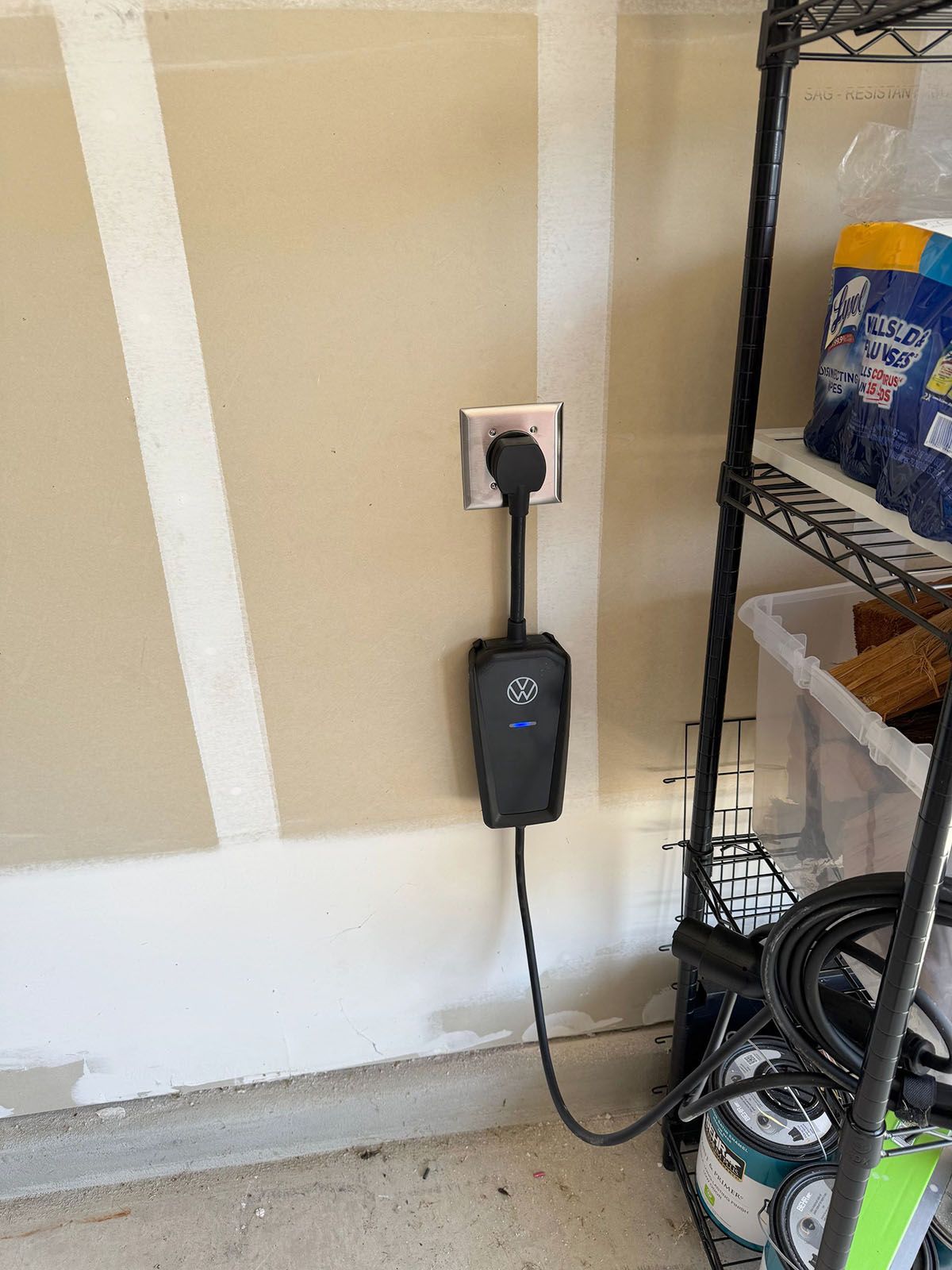 A black electric vehicle charging unit plugged into a wall outlet in a garage