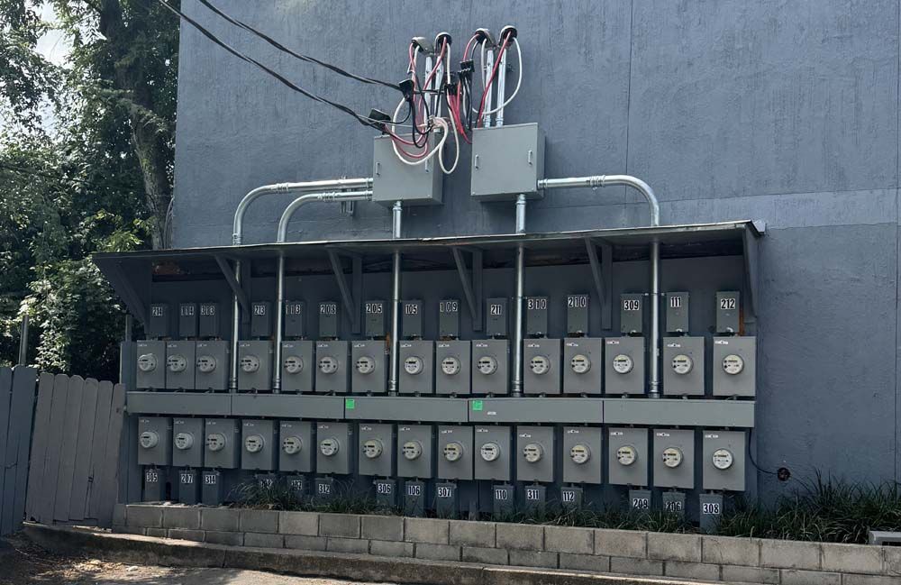 Electrical meters mounted on a gray building for multiple units, under a metal awning.