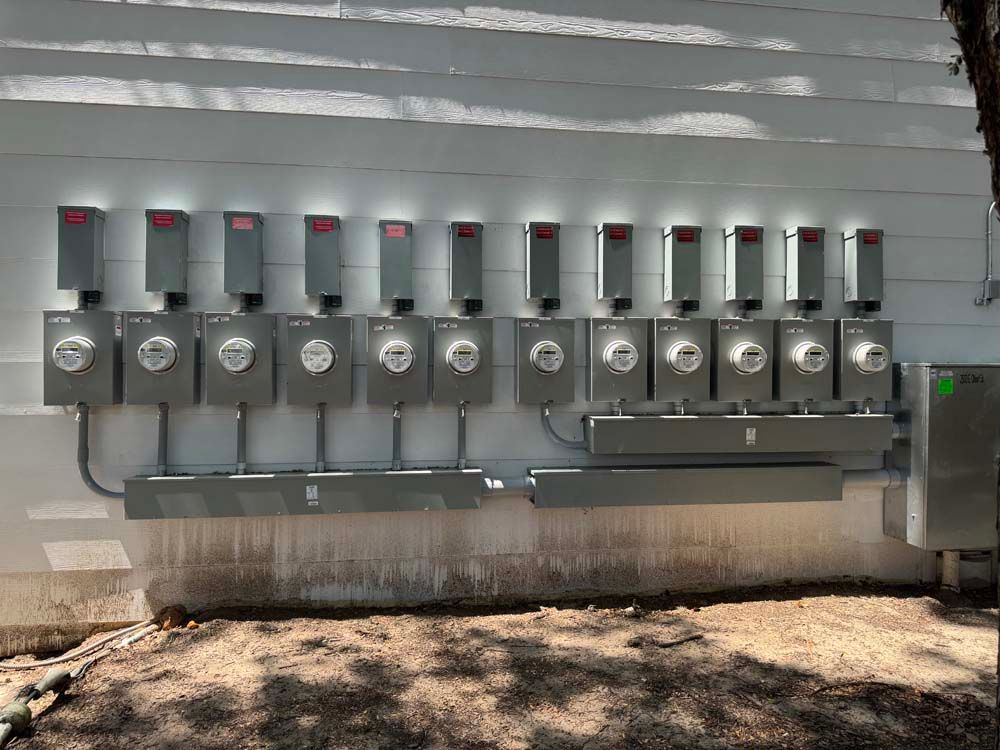 Exterior wall with a row of gray electrical meter boxes and conduits.
