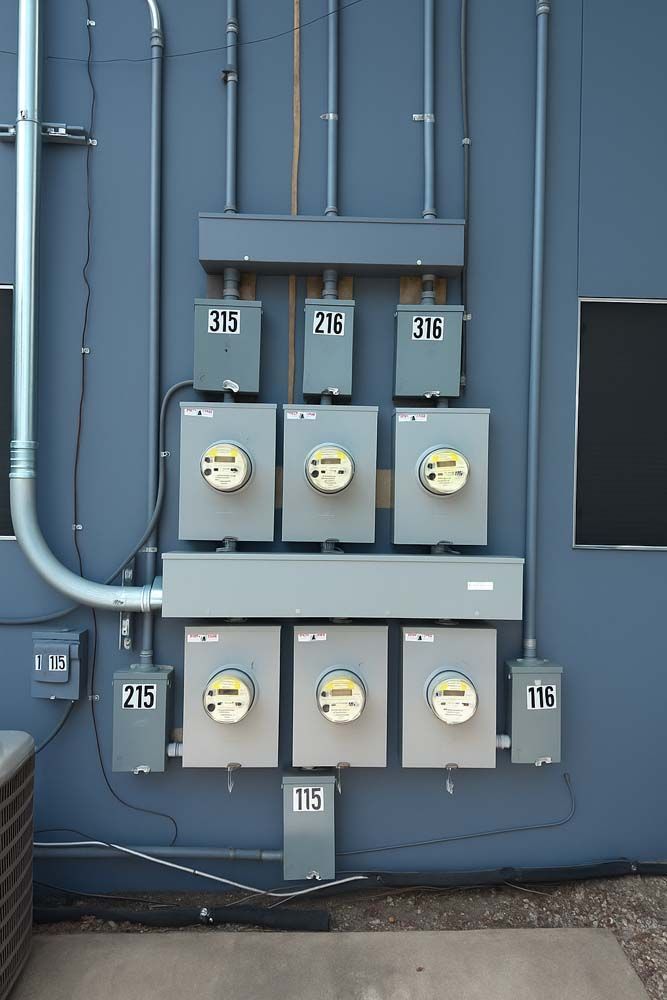 Exterior view of multiple electric meters on a building's white wall, with conduit.