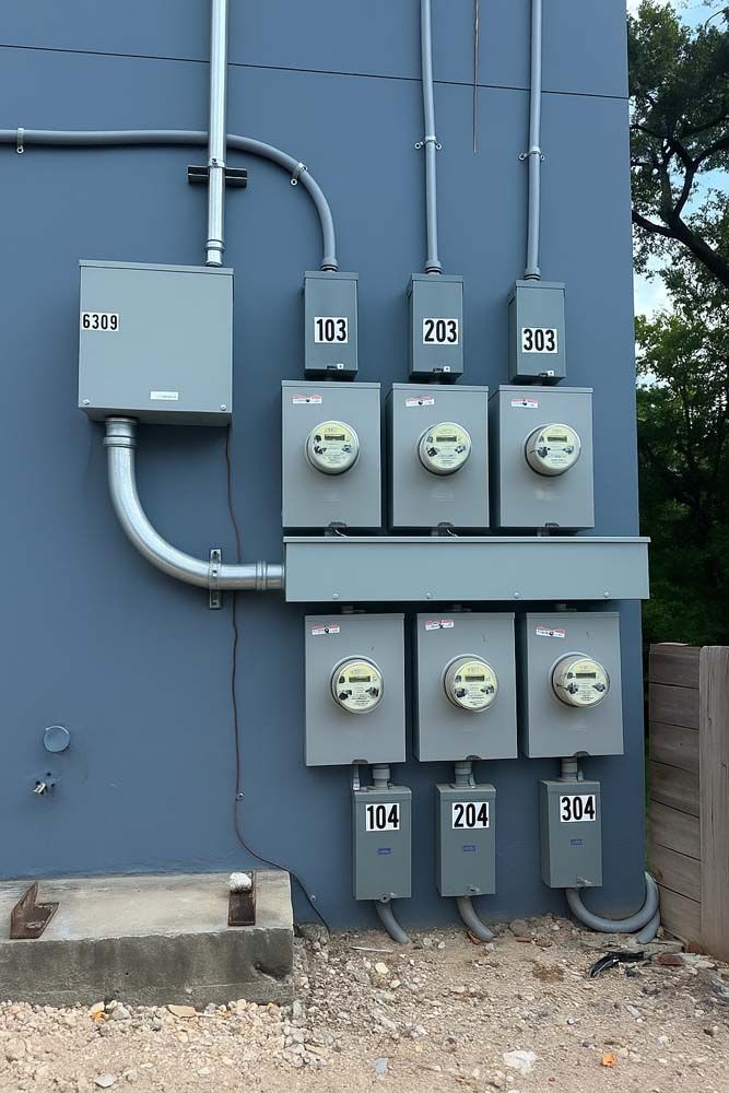 Gray electrical meters and boxes mounted on a blue building exterior.