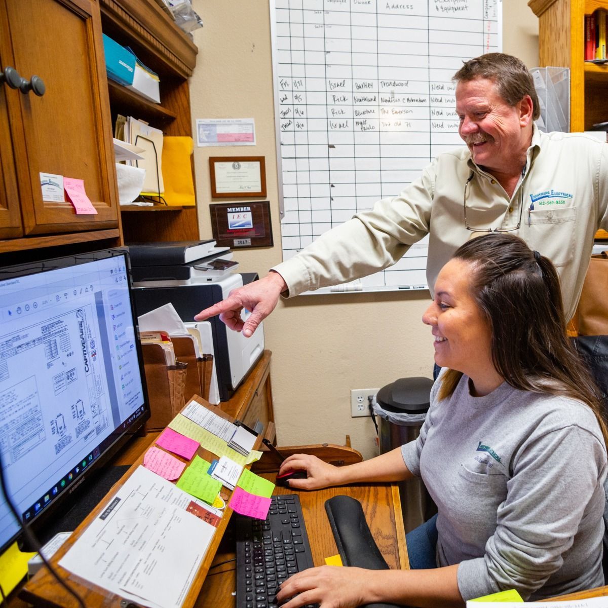A man is pointing at a computer screen while a woman is typing on a keyboard.