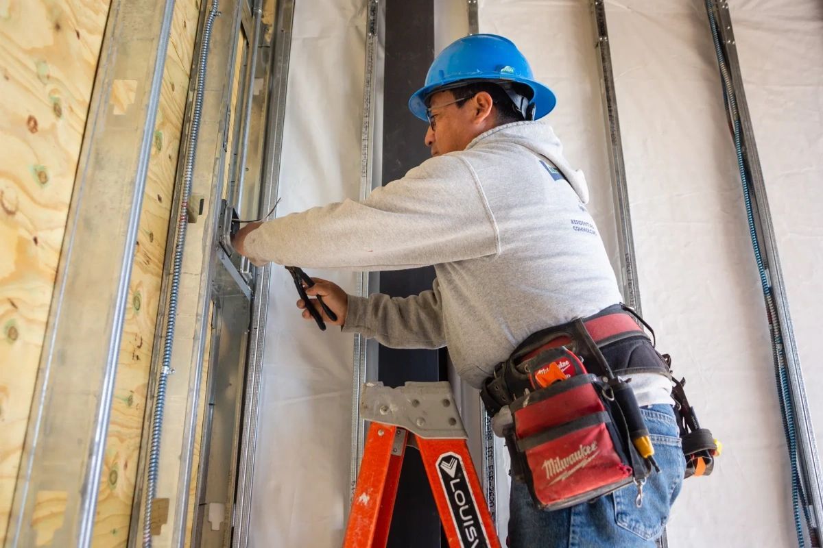 A man wearing a hard hat is working on a wall.