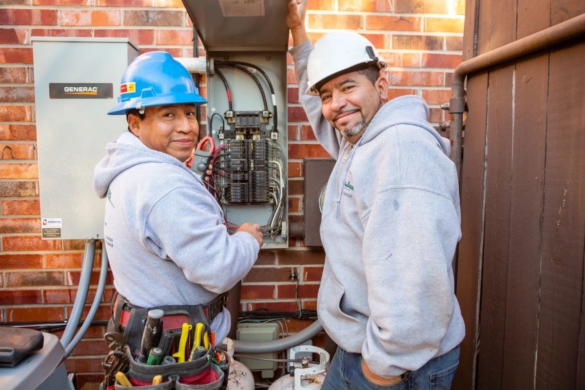 Two men wearing hard hats are working on an electrical box.