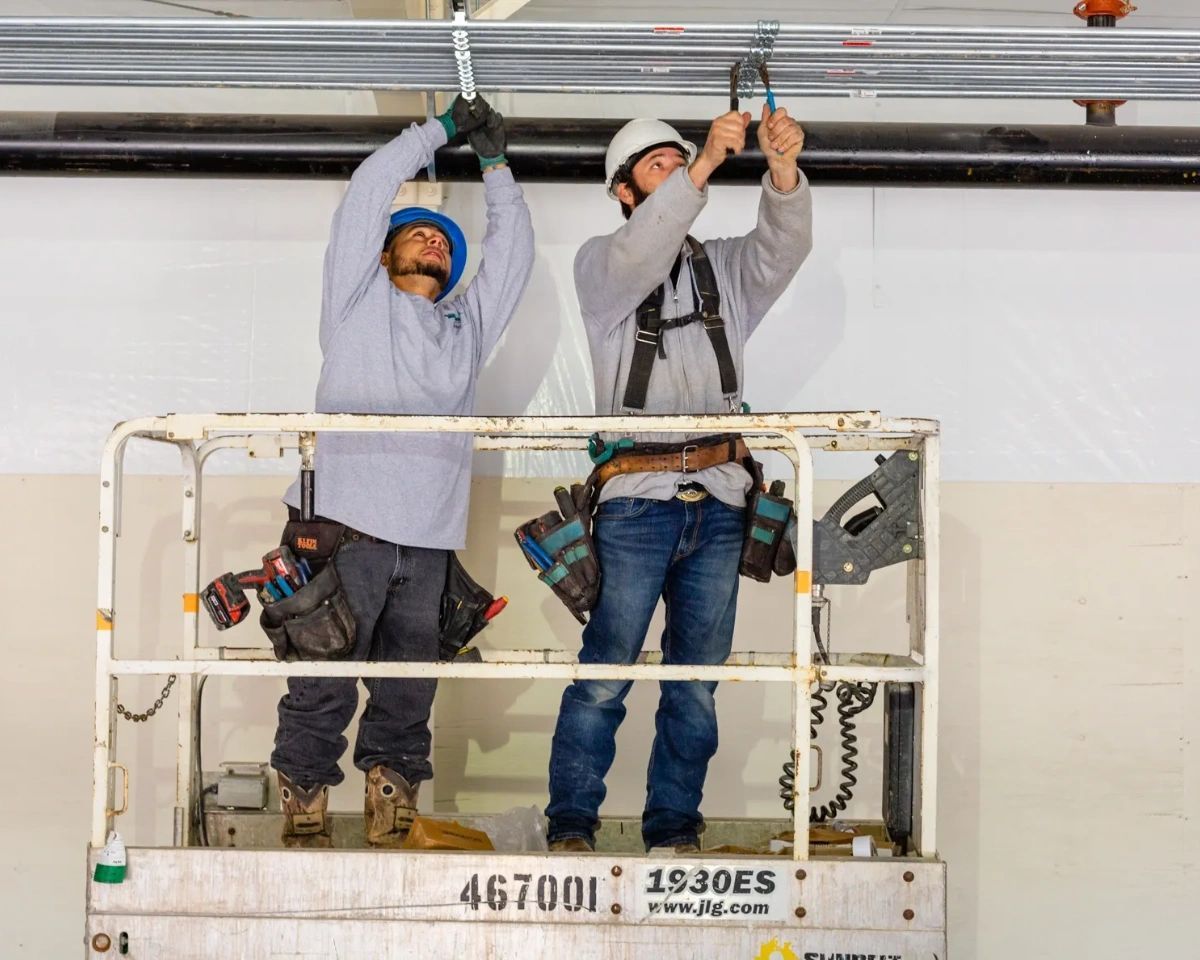 Two men are working on a ceiling on a lift.