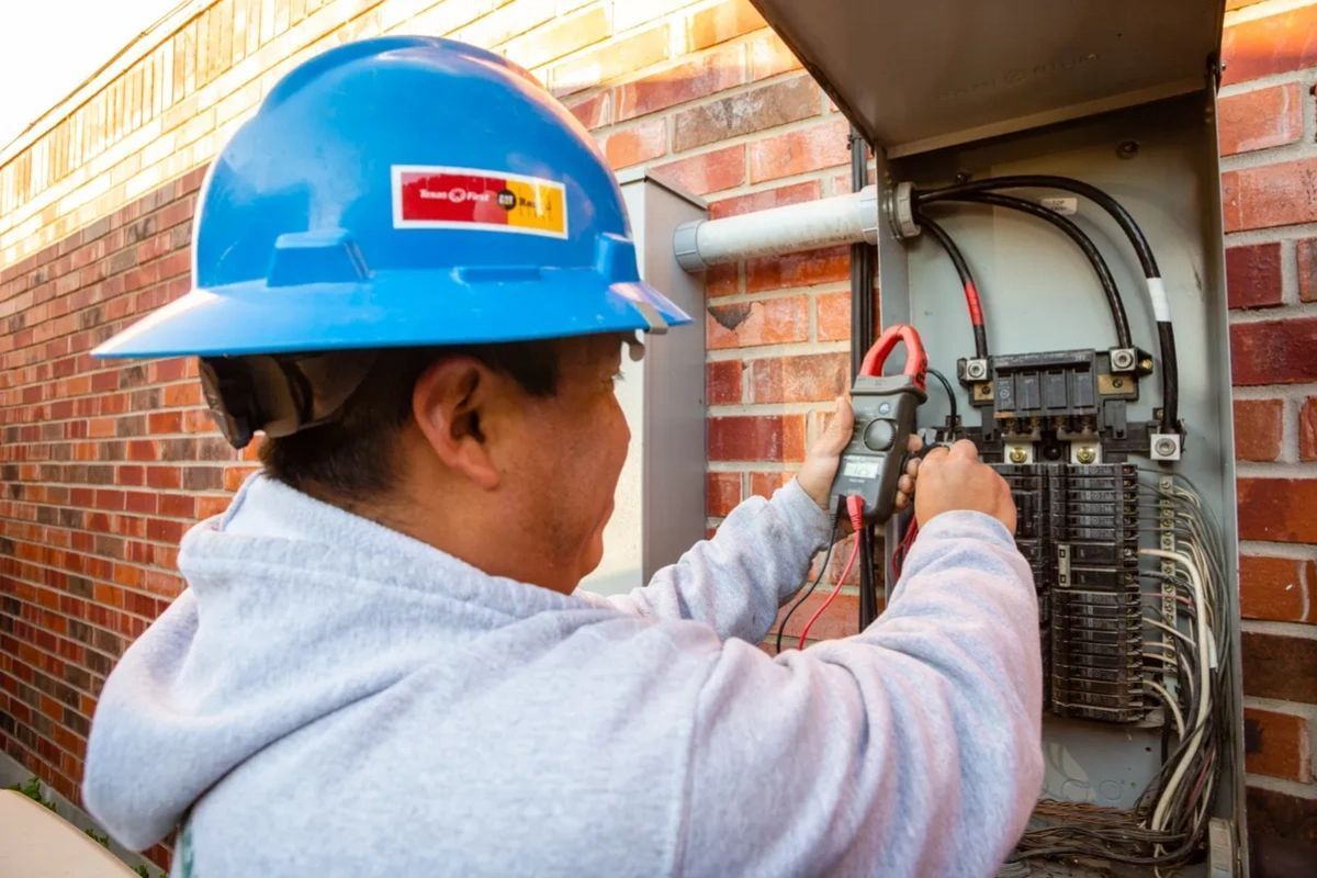A man wearing a blue hard hat is working on an electrical box.