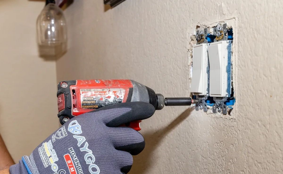 A person is using a drill to install a light switch.