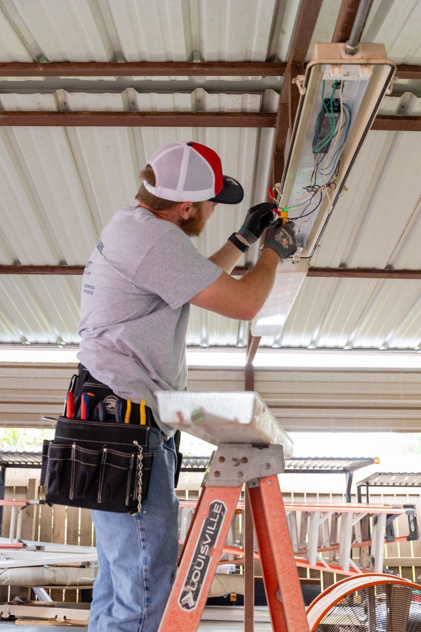 A man is standing on a ladder working on a light fixture.