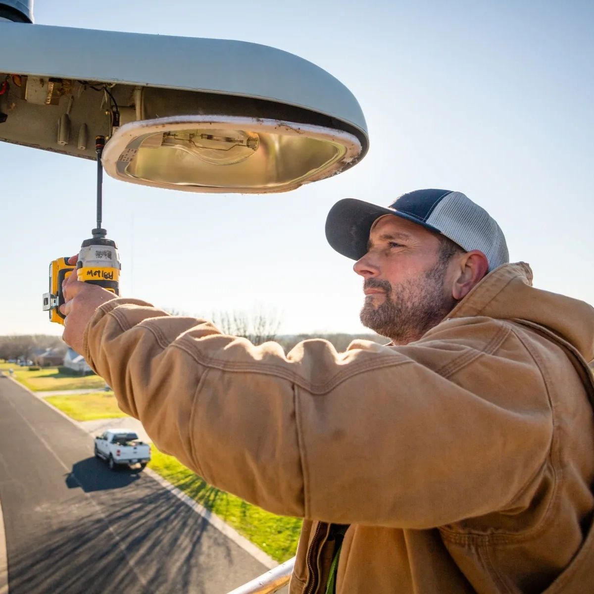 A man is working on a street light with a drill