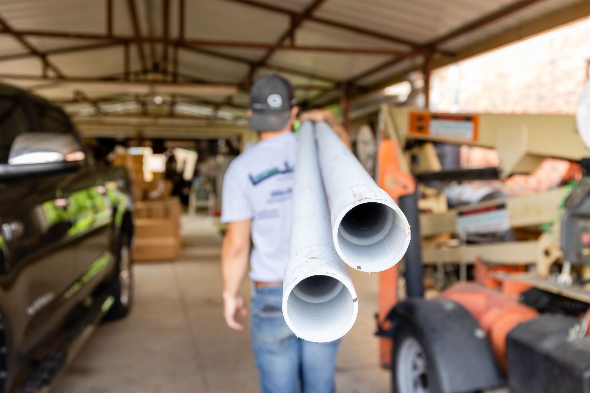 A man is carrying two white pipes in a garage.