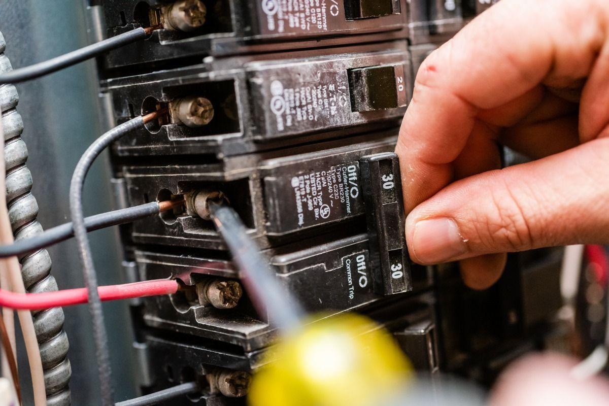 A person is working on an electrical box with a screwdriver.