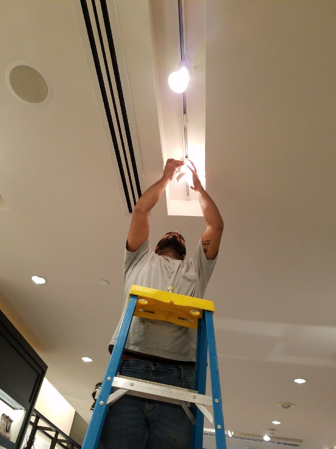 A man is standing on a ladder working on a light fixture.