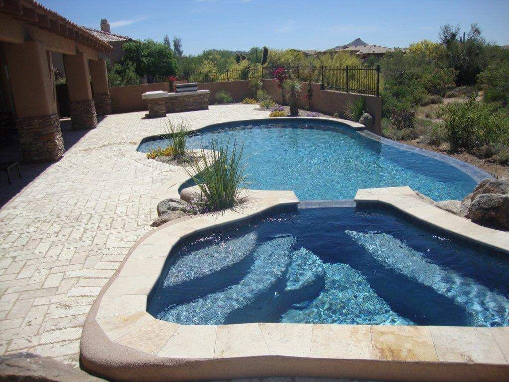 Pool and spa in a desert landscape with blue water and stone patio.