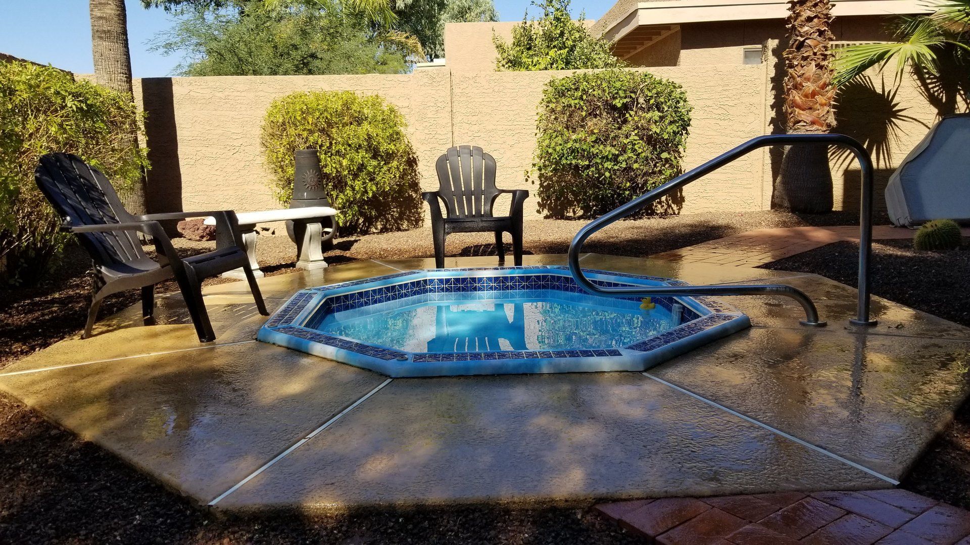 Hot tub with blue tile, chairs, and handrail in a yard.