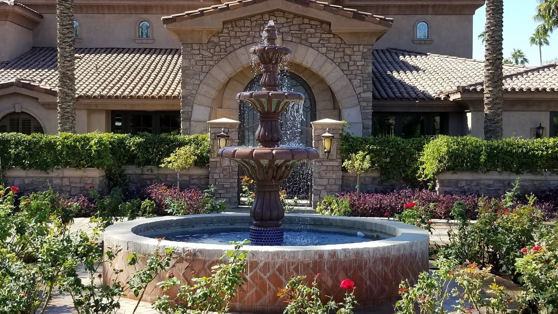 Fountain in a garden, in front of a building with a terracotta roof.