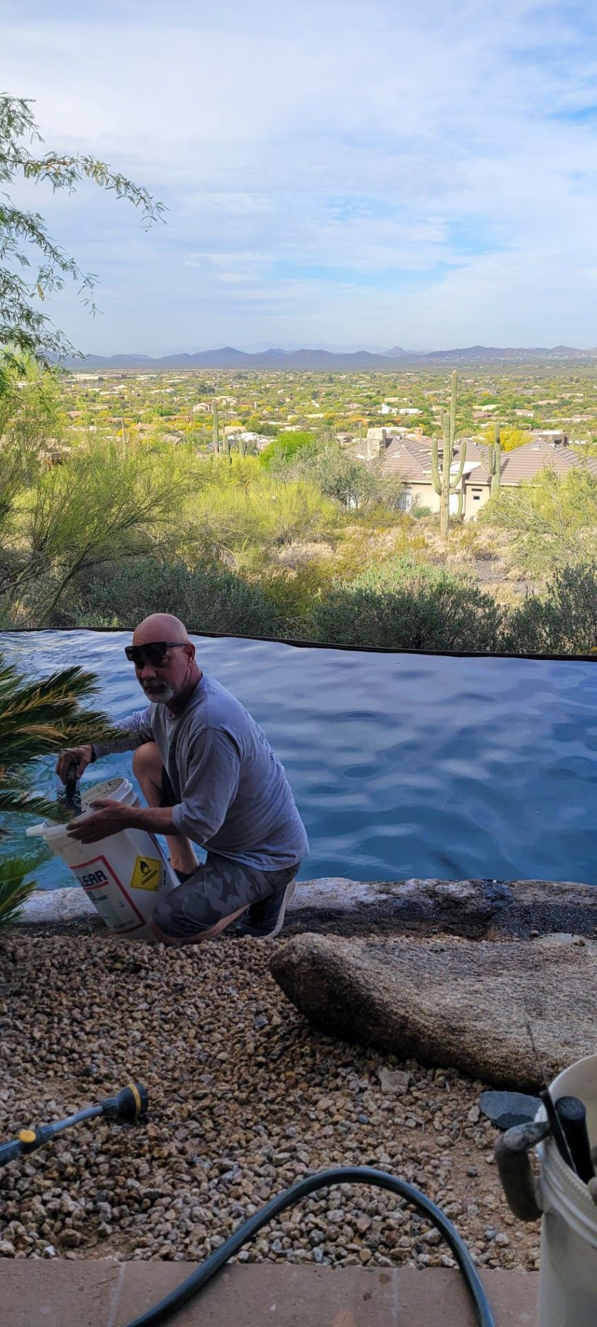 Man crouches by a pool with a scenic landscape in the background.