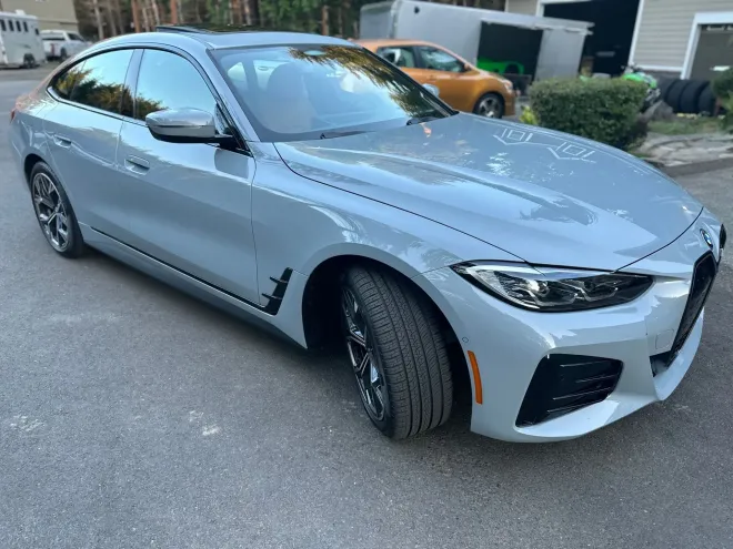 Gray BMW sedan parked on asphalt. Black accents, chrome wheels, green lawn, trees in background.