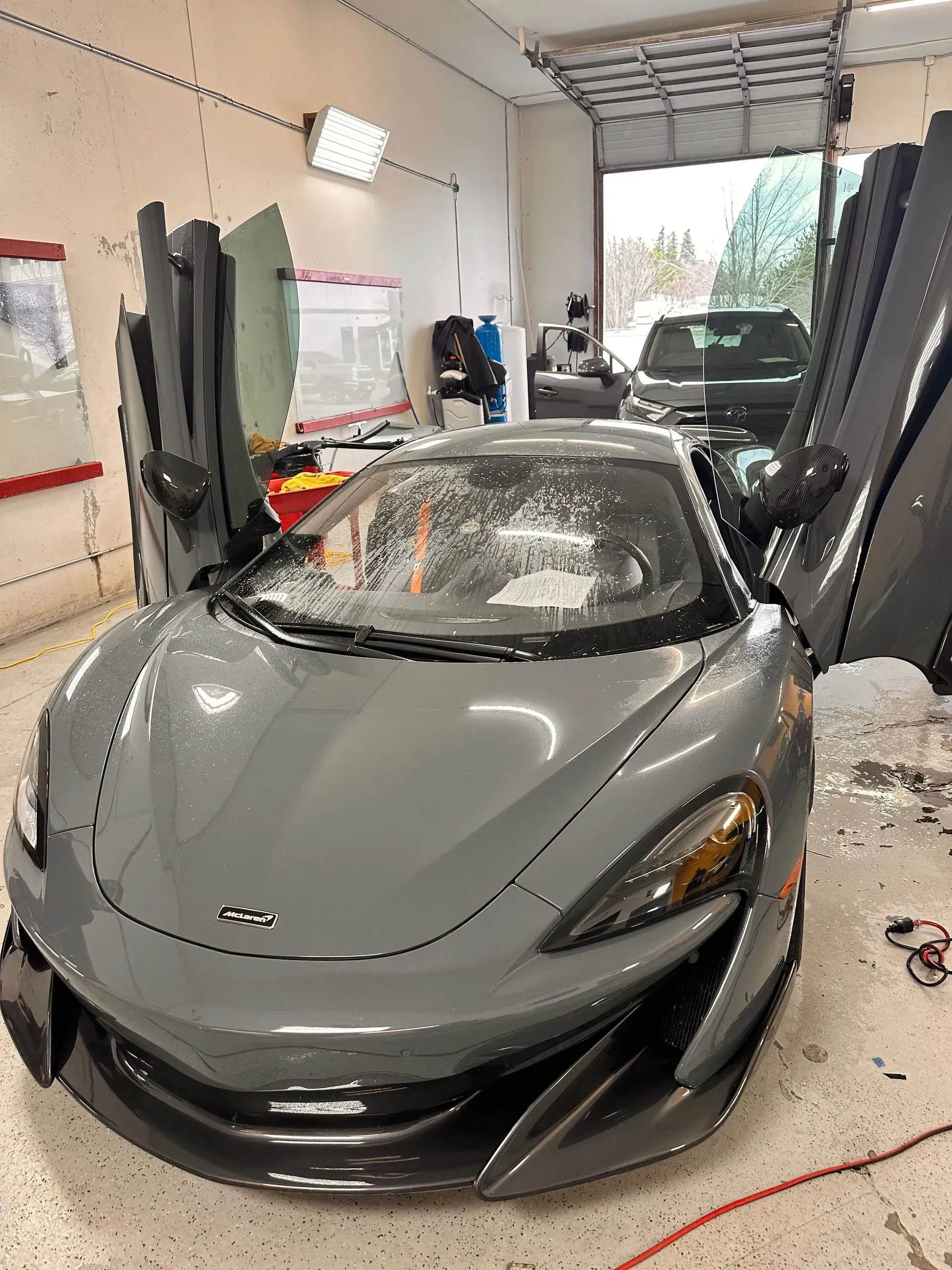Gray McLaren sports car with doors open, inside a garage.