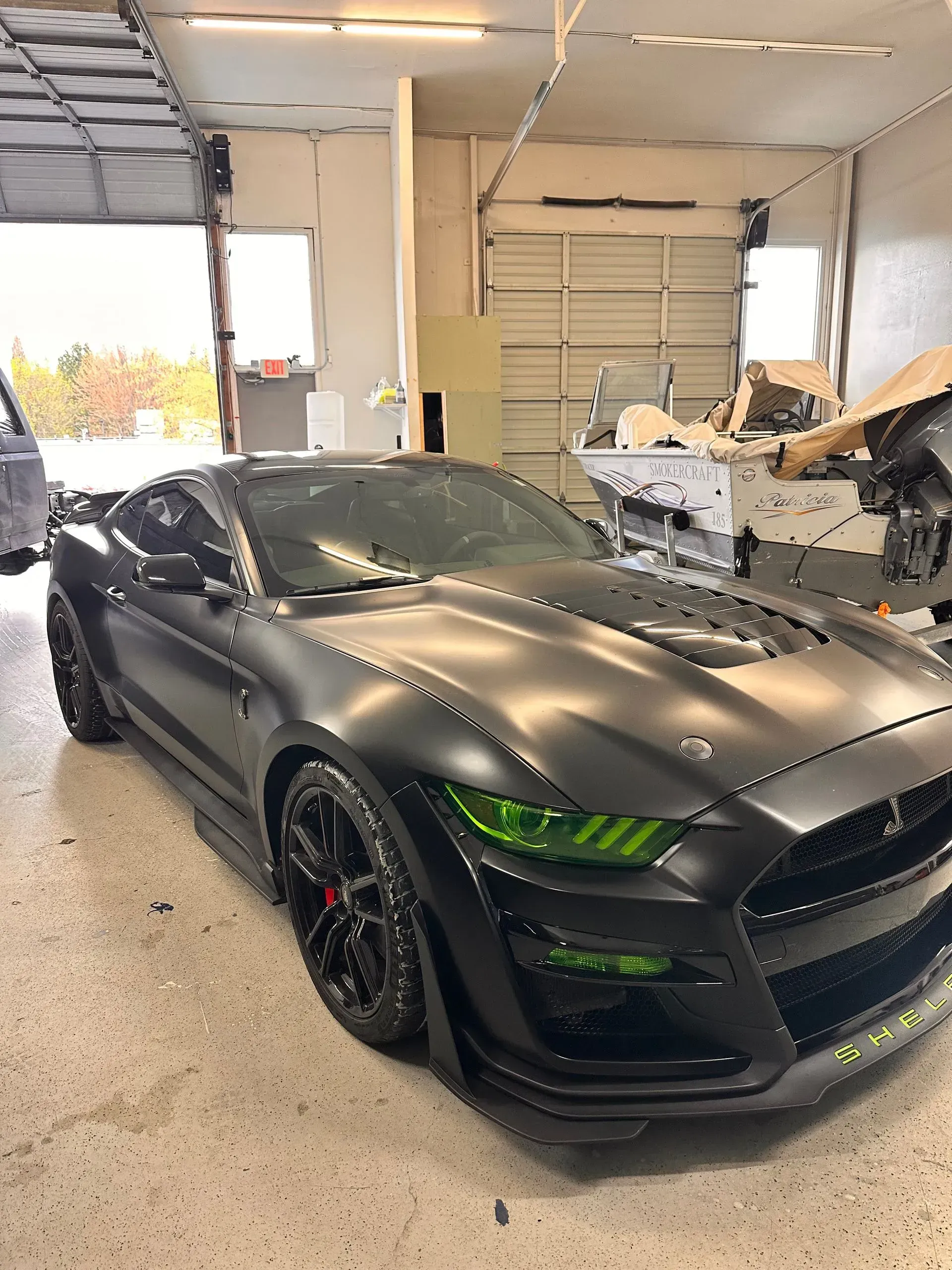 Black Mustang sports car with green accents in a garage, possibly being worked on.