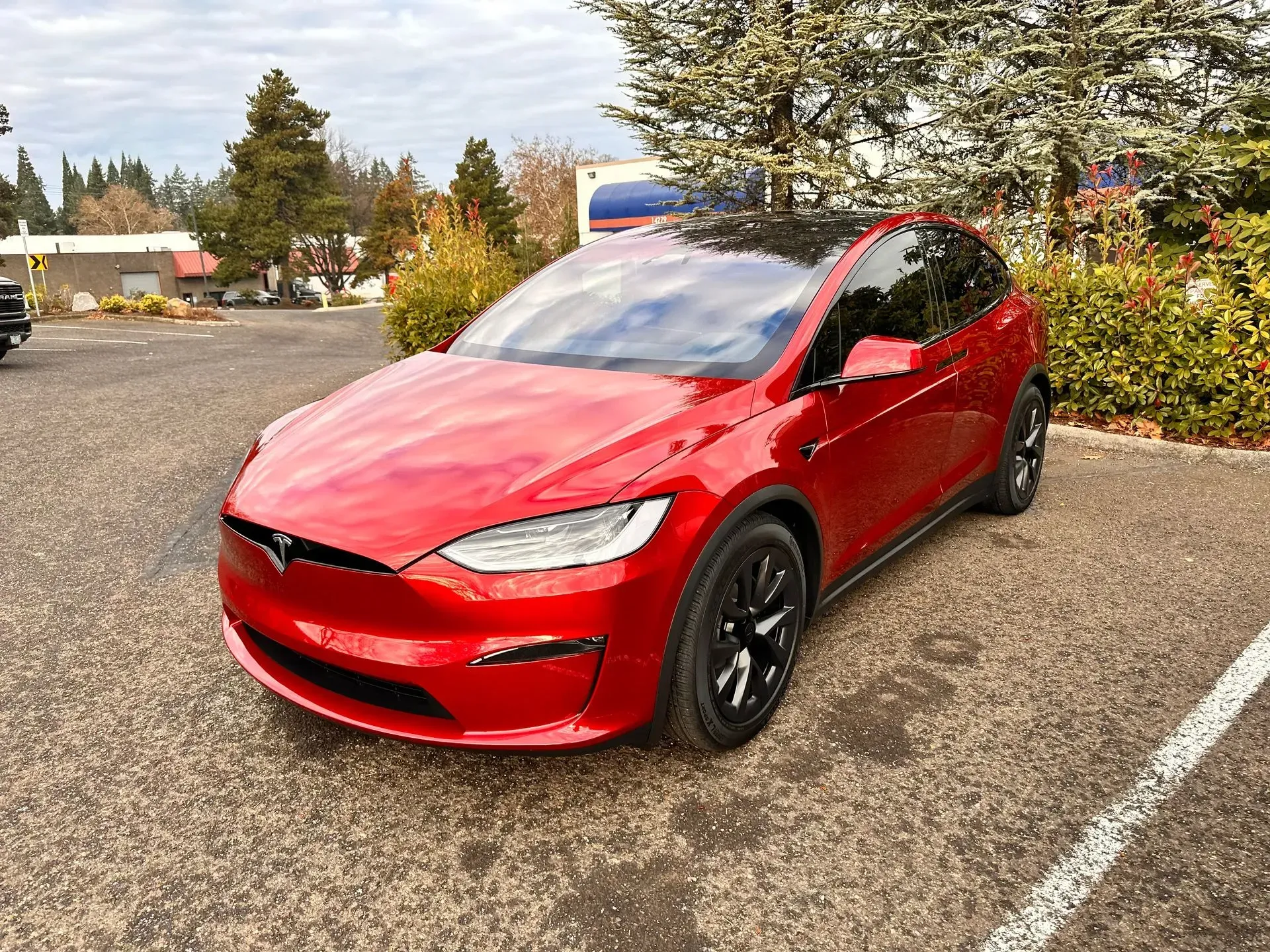 Red Tesla Model X car parked outside, black roof and wheels.