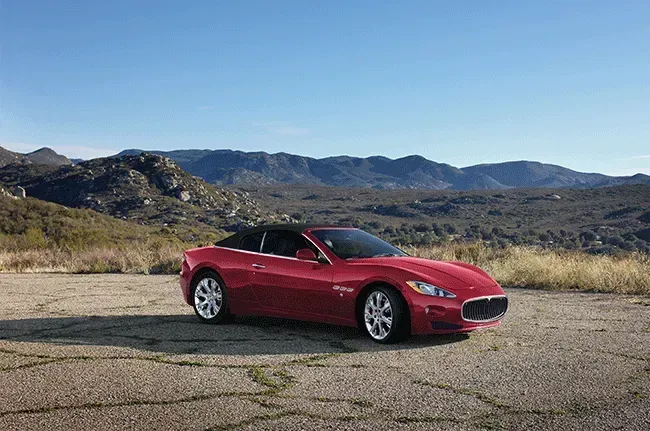 Red convertible car parked on a cracked road, with mountains and blue sky in the background.