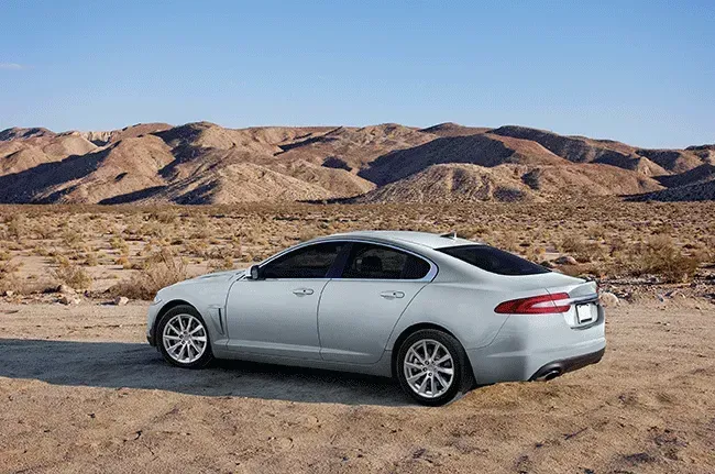 Silver Jaguar sedan parked on dirt road in desert landscape.