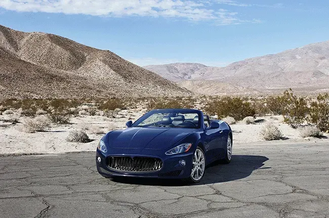 Blue convertible car parked on a cracked road in a desert landscape.