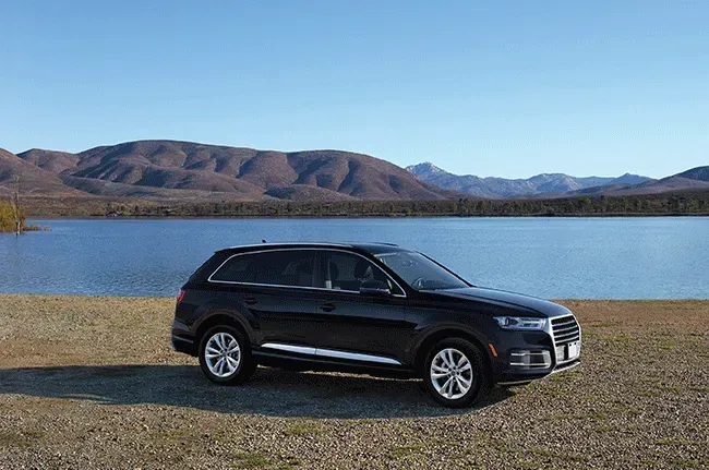 Black SUV parked by lake with mountains in the background under a blue sky.