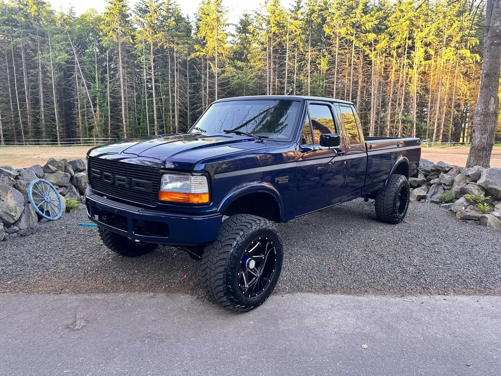 Blue lifted Ford pickup truck with black wheels parked outdoors.