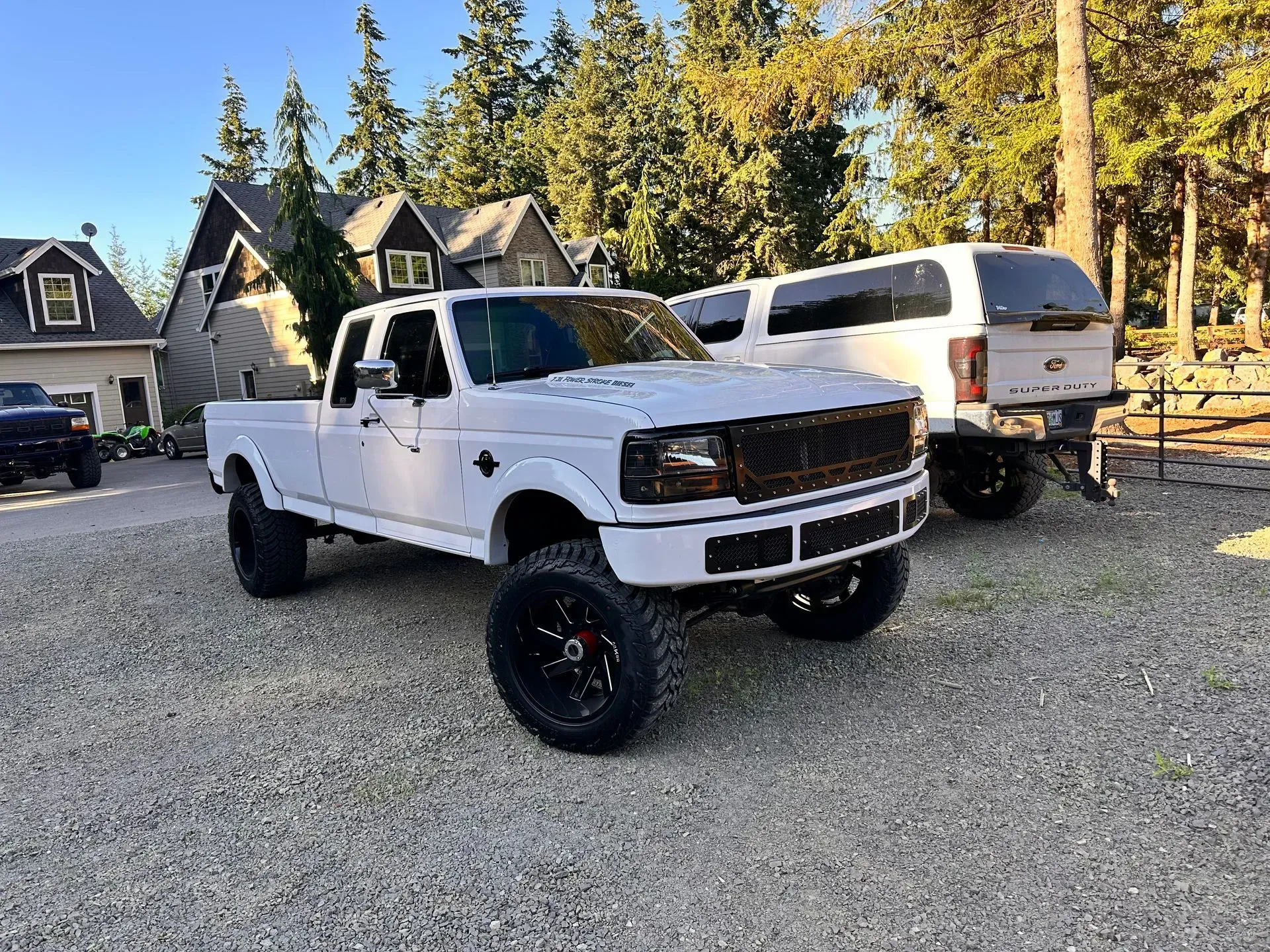 White lifted pickup truck with black wheels parked on gravel driveway.