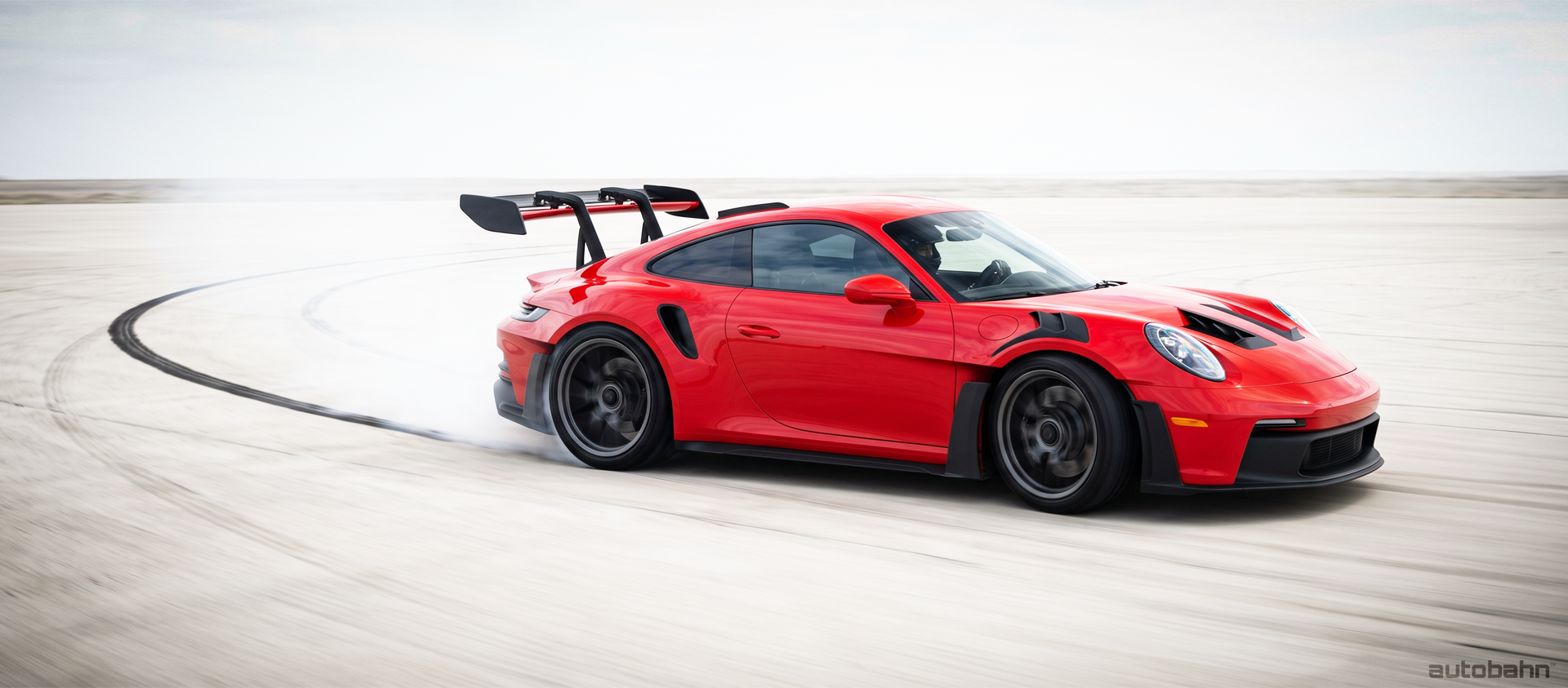 Red sports car drifting on a bright racetrack, leaving tire marks and smoke behind.