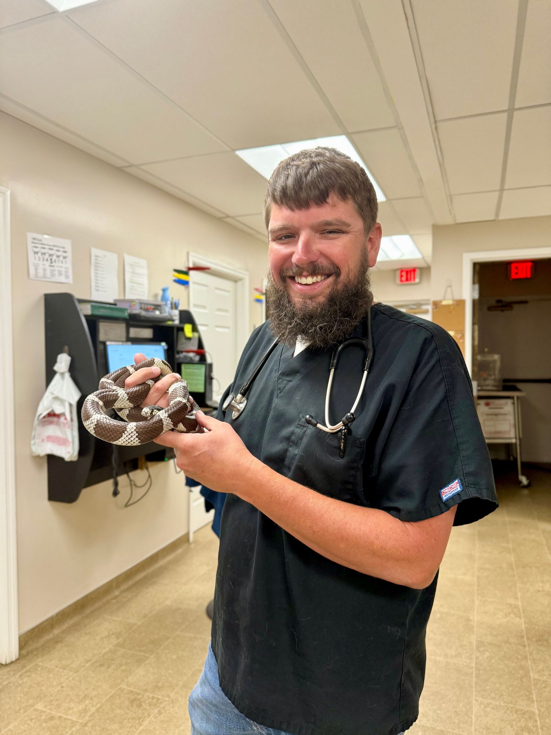 Smiling man in dark scrubs holding a snake in a hospital hallway