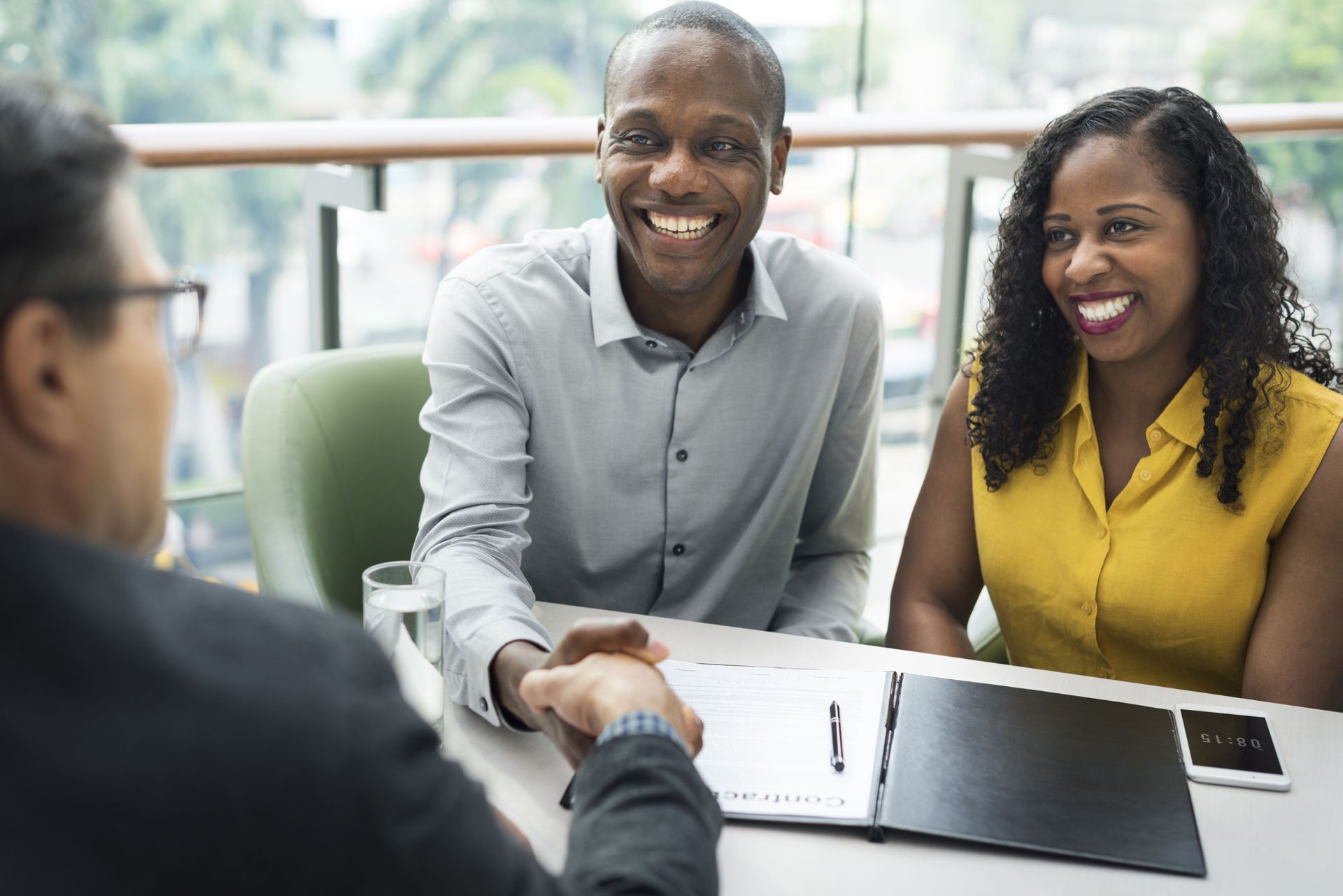 Two people smiling and shaking hands across a table in a bright office meeting
