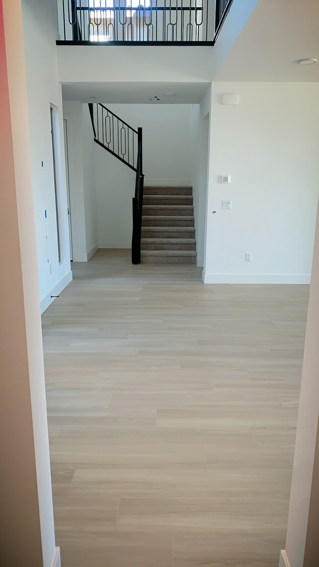 Entryway with wood-look flooring, stairs leading up, and a balcony overhead. White walls and black railing.