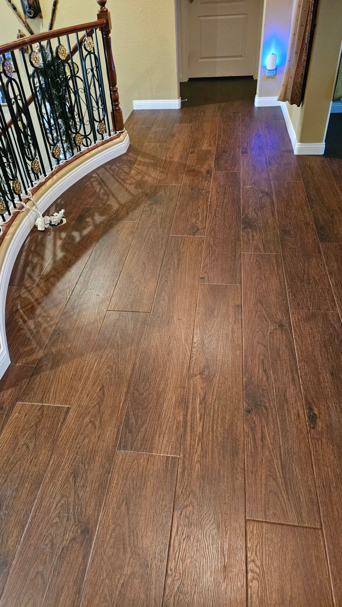 Brown wooden floor with cracks, a curved staircase, and a doorway leading to another room.