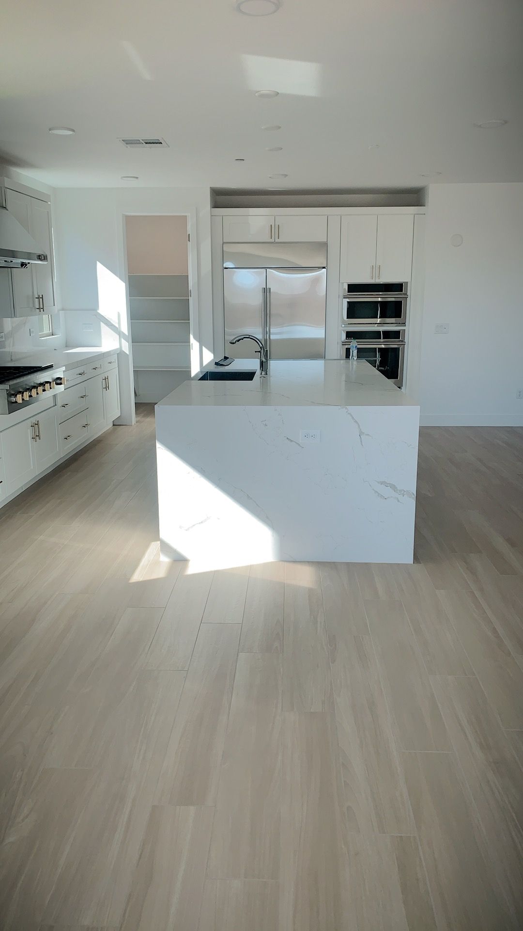 Bright white kitchen with a marble island and light wood floors.